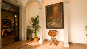 A hallway with a tiled floor, a potted plant, a wooden cabinet, and a framed painting on the wall. - Hotel Gli Orzali (Firenzuola)