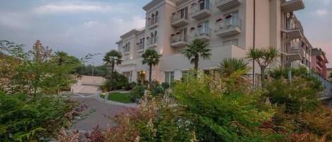 A multi-story hotel with balconies, surrounded by lush greenery and a well-maintained garden.
