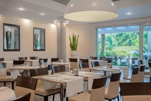 Un comedor moderno con mesas, sillas, ventanas amplias y una lámpara en el techo.