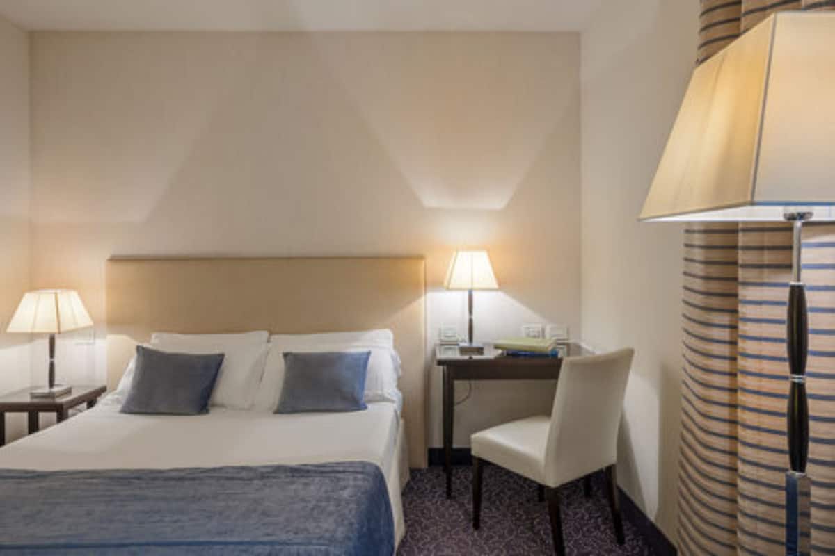 Habitación de hotel con cama, dos lámparas de noche, un escritorio con silla y una cortina a rayas.