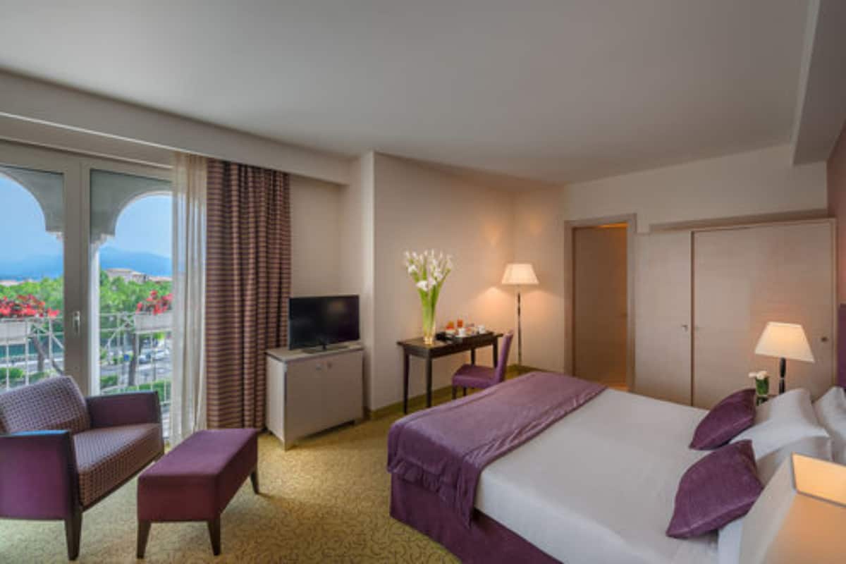 Habitación de hotel con cama, televisión, escritorio, silla, lámpara y vista al exterior.