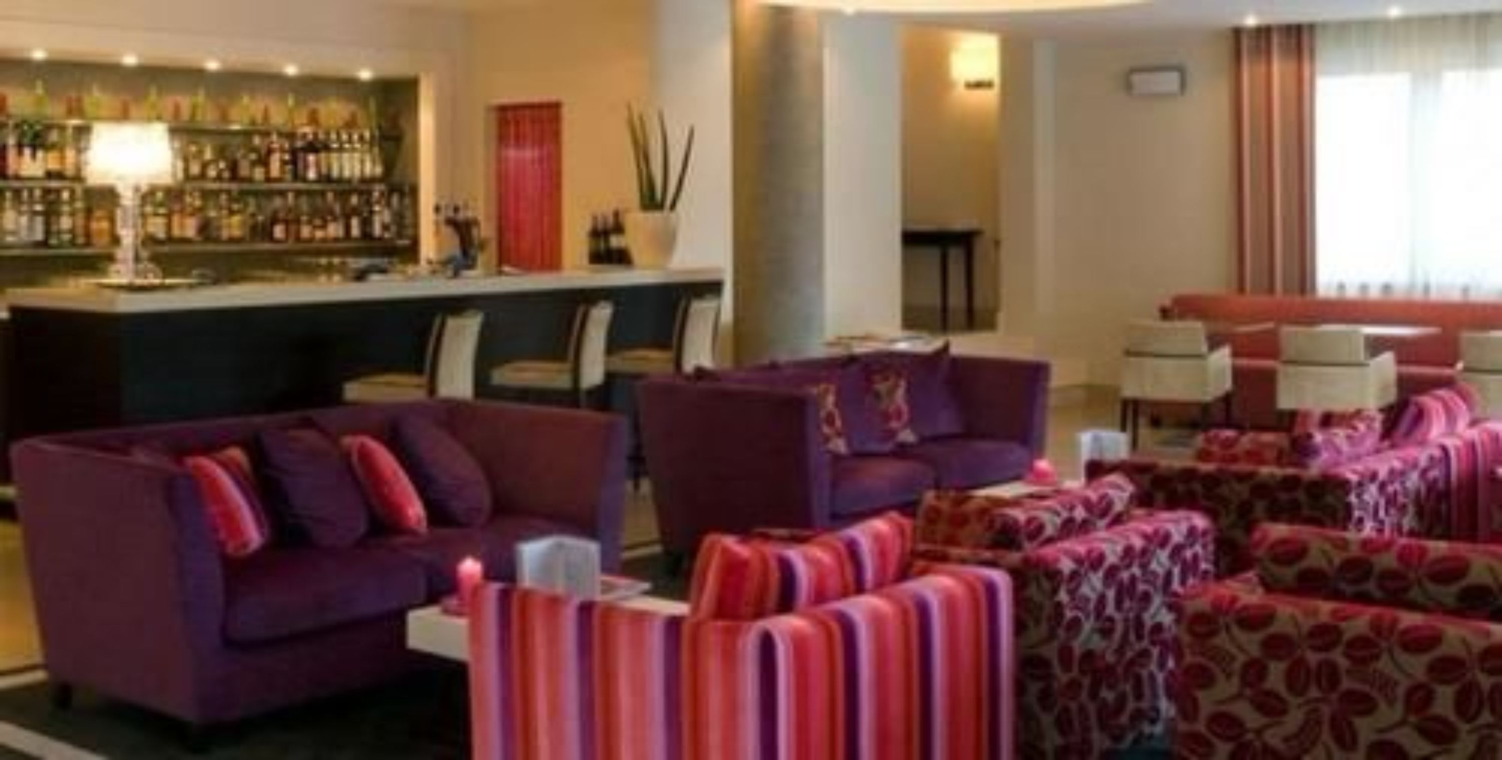 Een hotel lobby met paarse banken, een bar met verschillende flessen en een zithoek met gestreepte kussens.