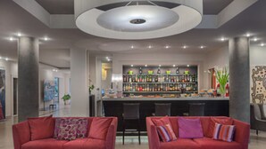 Een moderne lobby met twee rode banken, een barruimte met diverse flessen en een grote ronde lamp aan het plafond.