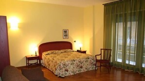 Een hotelkamer met een bed, een stoel, een nachtkastje en een lamp.