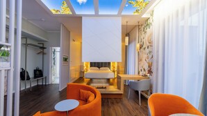 A modern hotel room with a skylight, a bed, orange chairs, a small table, and a shower area. - Hotel Salus Terme - Adults Only (Viterbo)