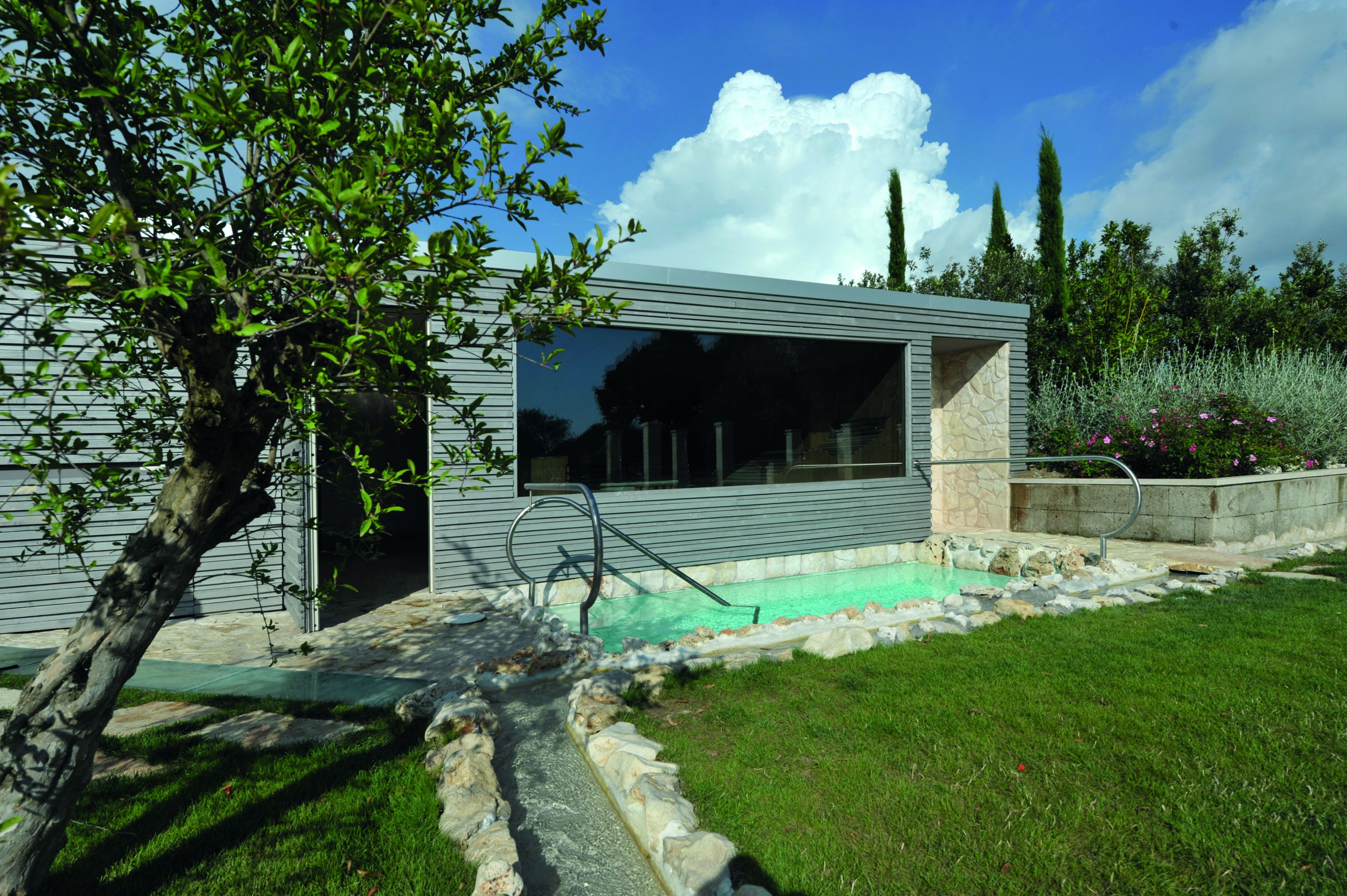 Una casa moderna con piscina, un camino de piedra y un césped cuidado.