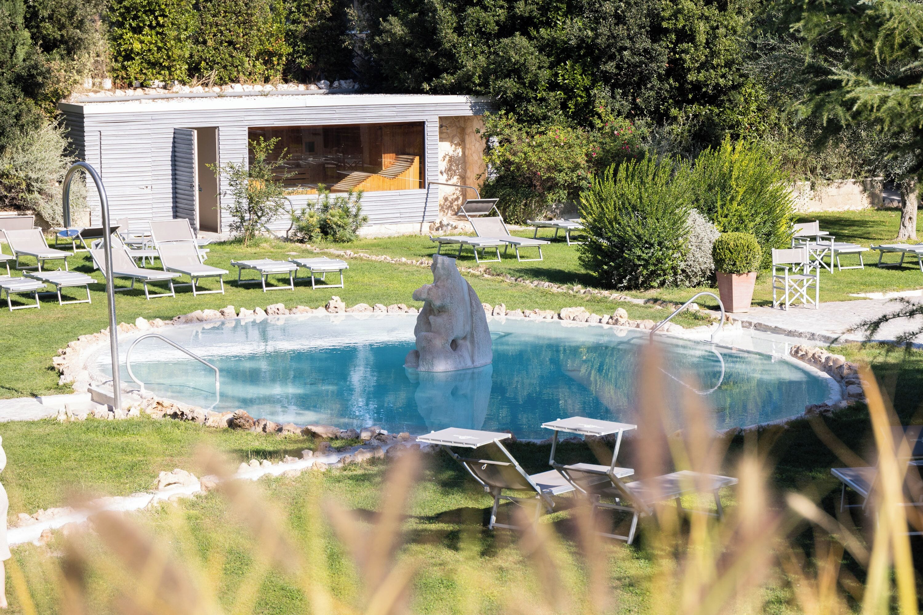 A swimming pool with a dolphin sculpture, surrounded by lounge chairs and a building with a glass facade.