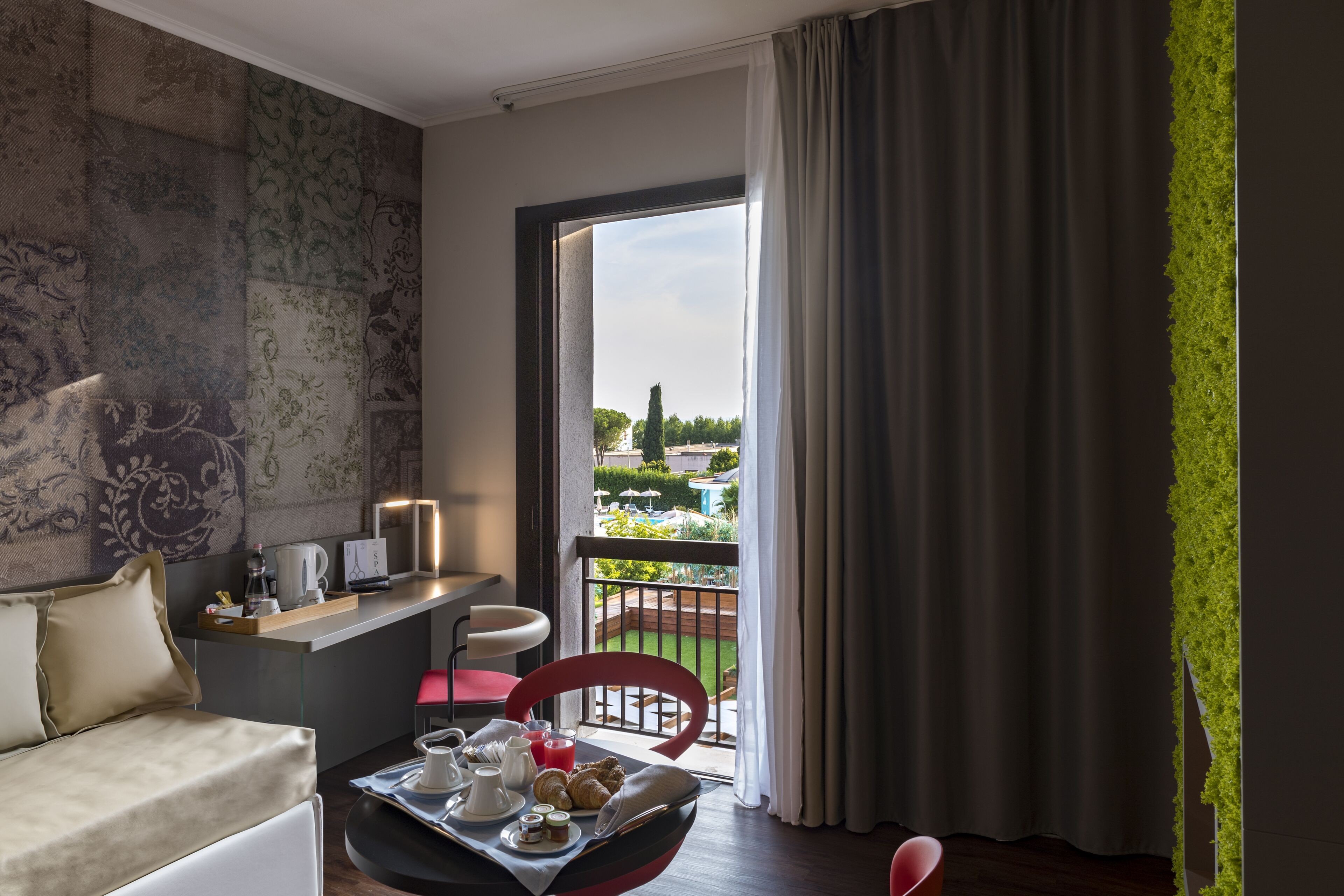 A modern hotel room with a balcony, a dining area with breakfast items, and a view of the garden.