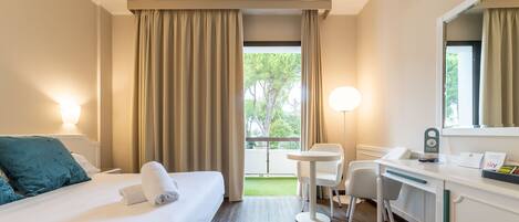 A hotel room with a bed, desk, chairs, and a view of the outdoors.