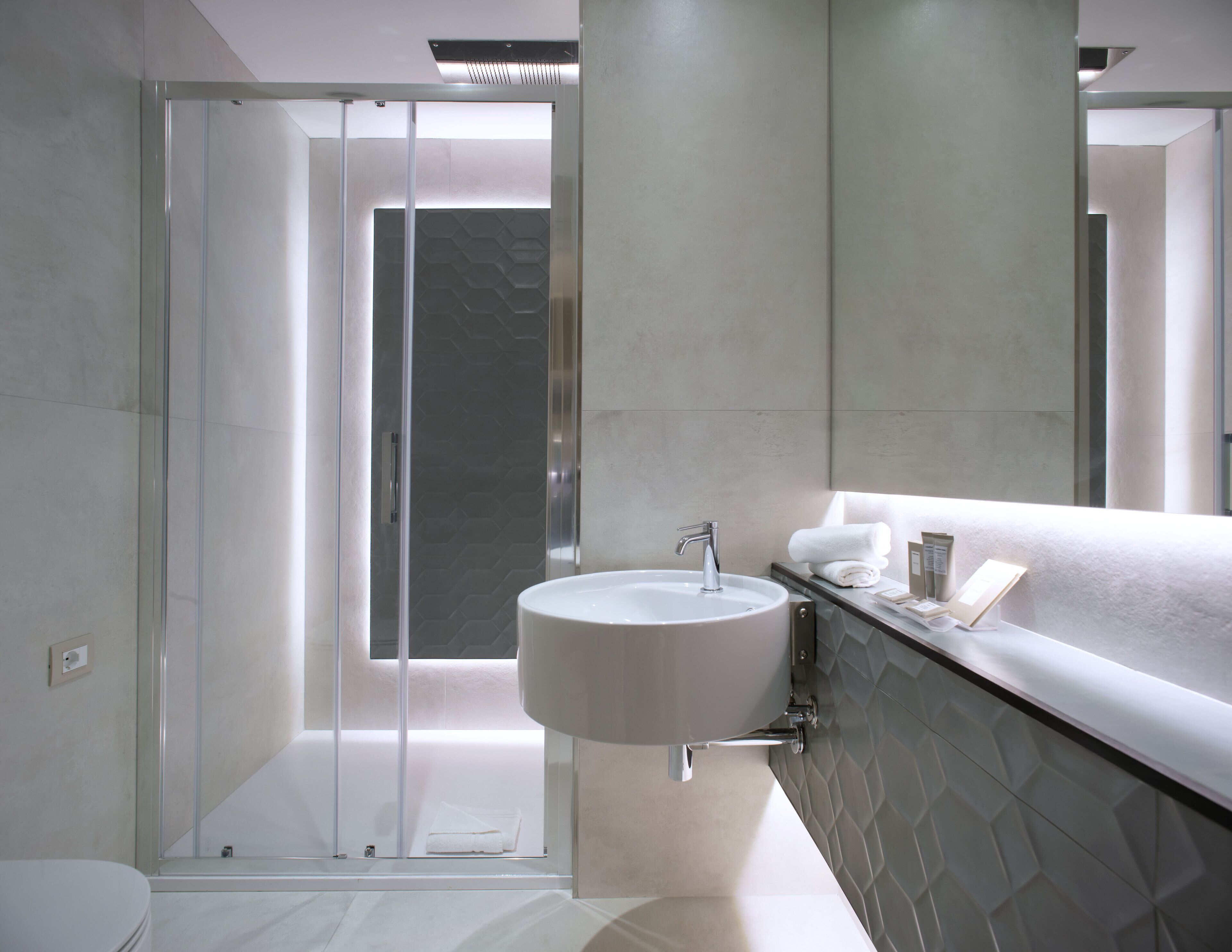 A modern bathroom with a glass shower enclosure, a white sink, and a large mirror.