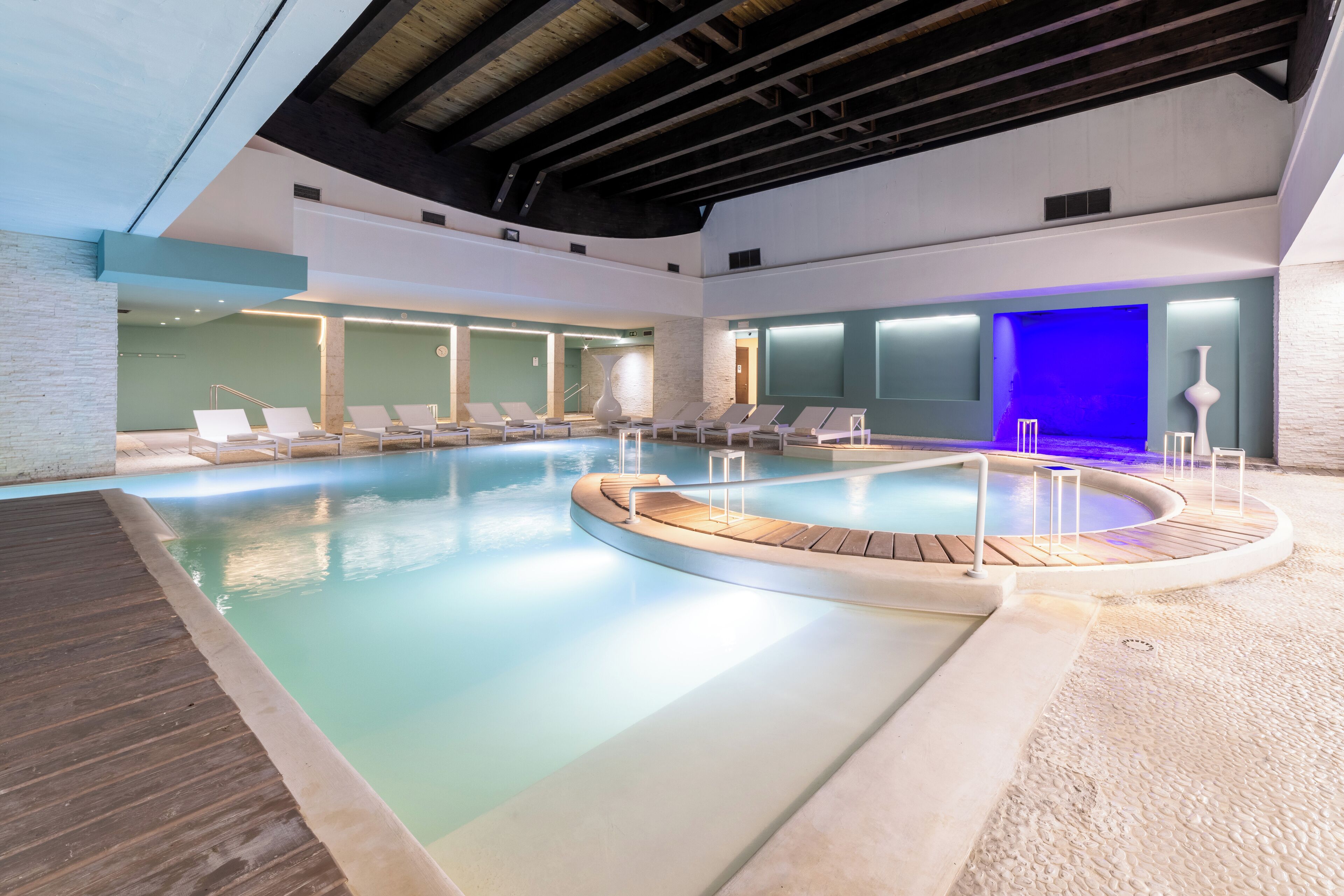 An indoor swimming pool with lounge chairs and a wooden deck.