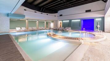 An indoor swimming pool with lounge chairs and a wooden deck.