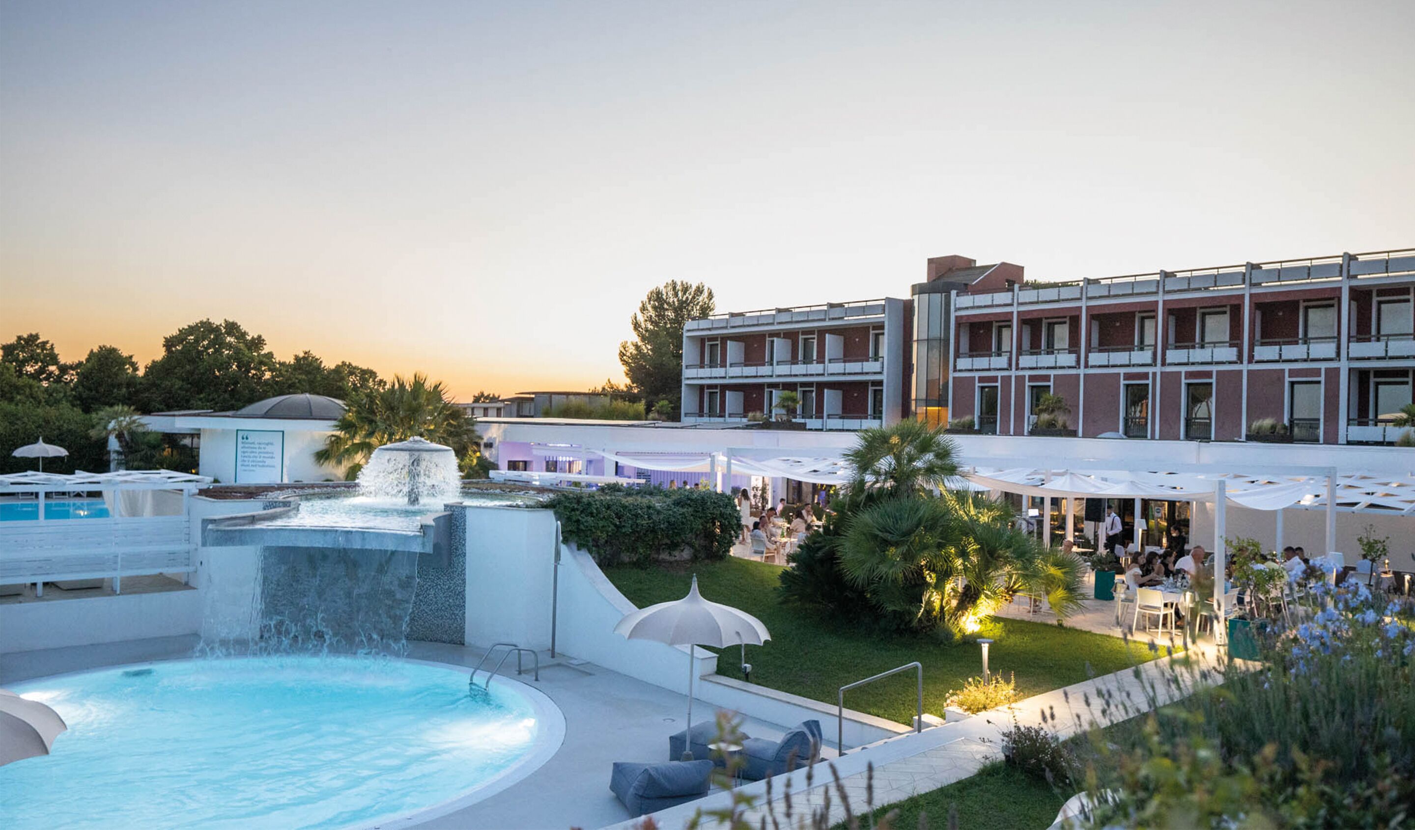 Un hotel con piscina, zona de comedor exterior y una fuente.