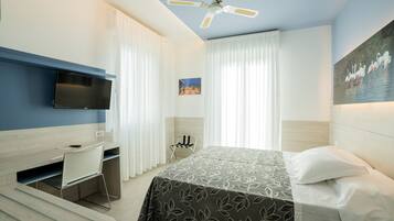 A hotel room with a bed, a desk, a chair, a television, and a painting on the wall.