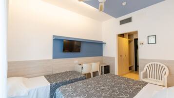 A hotel room with two beds, a desk, a chair, a TV, and a ceiling fan.