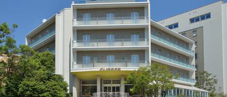 A multi-story hotel with a central entrance, balconies, and a clear sky.