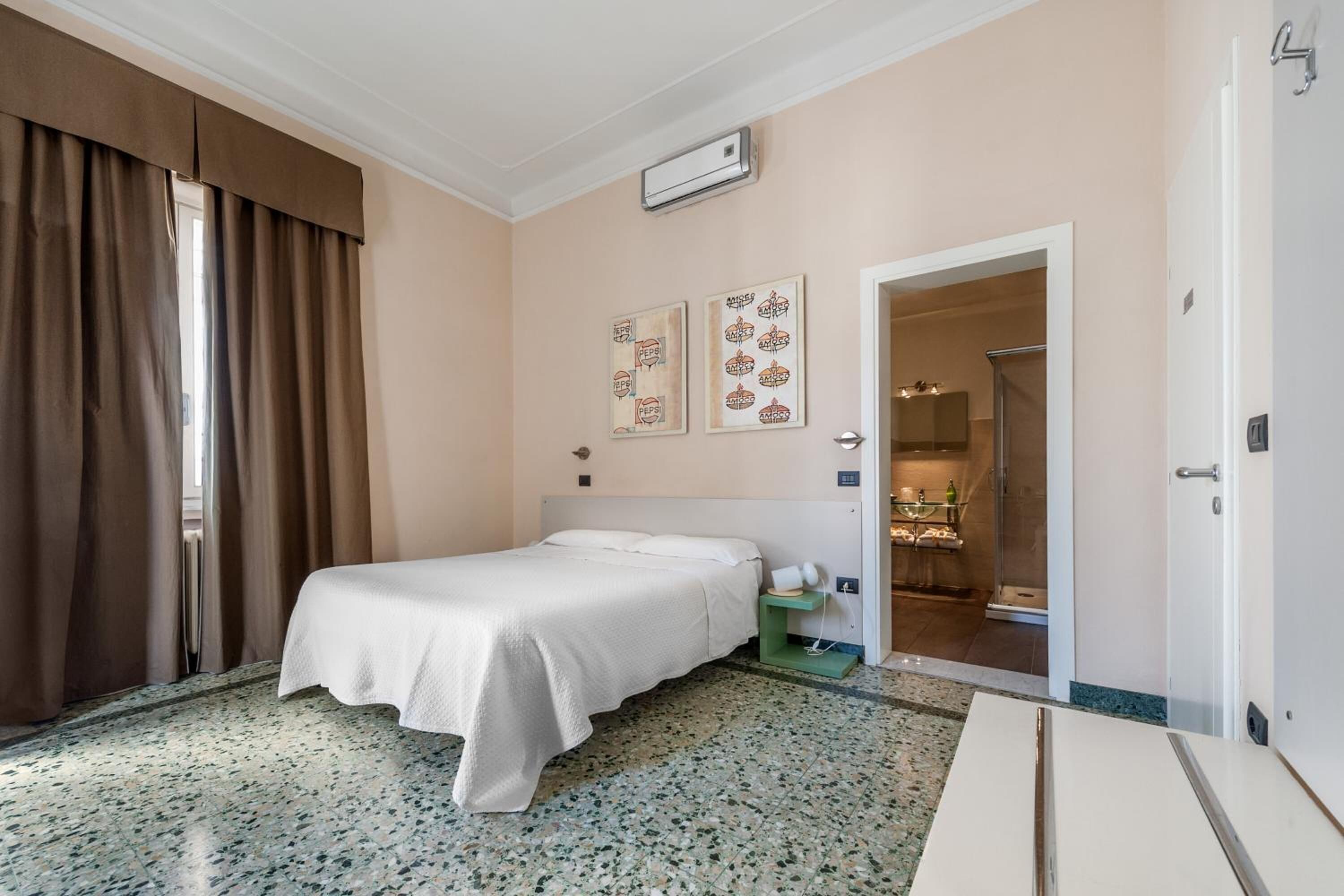 A hotel room with a bed, a small table, a nightstand, a mirror, and a door leading to a bathroom.