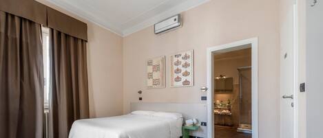 A hotel room with a bed, a small table, a nightstand, a mirror, and a door leading to a bathroom.