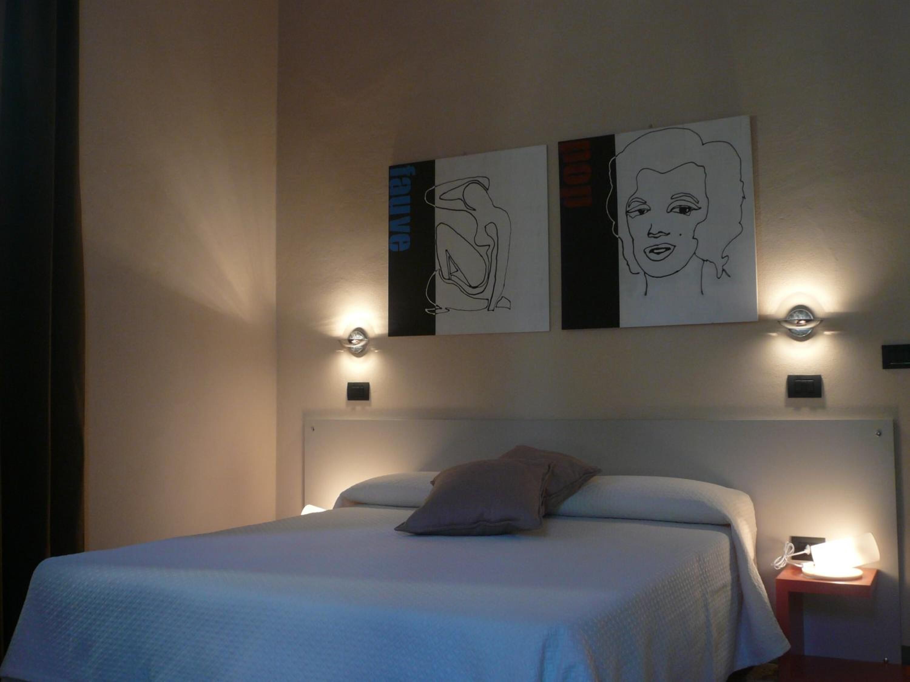 A hotel room with a bed, a nightstand, and wall art.
