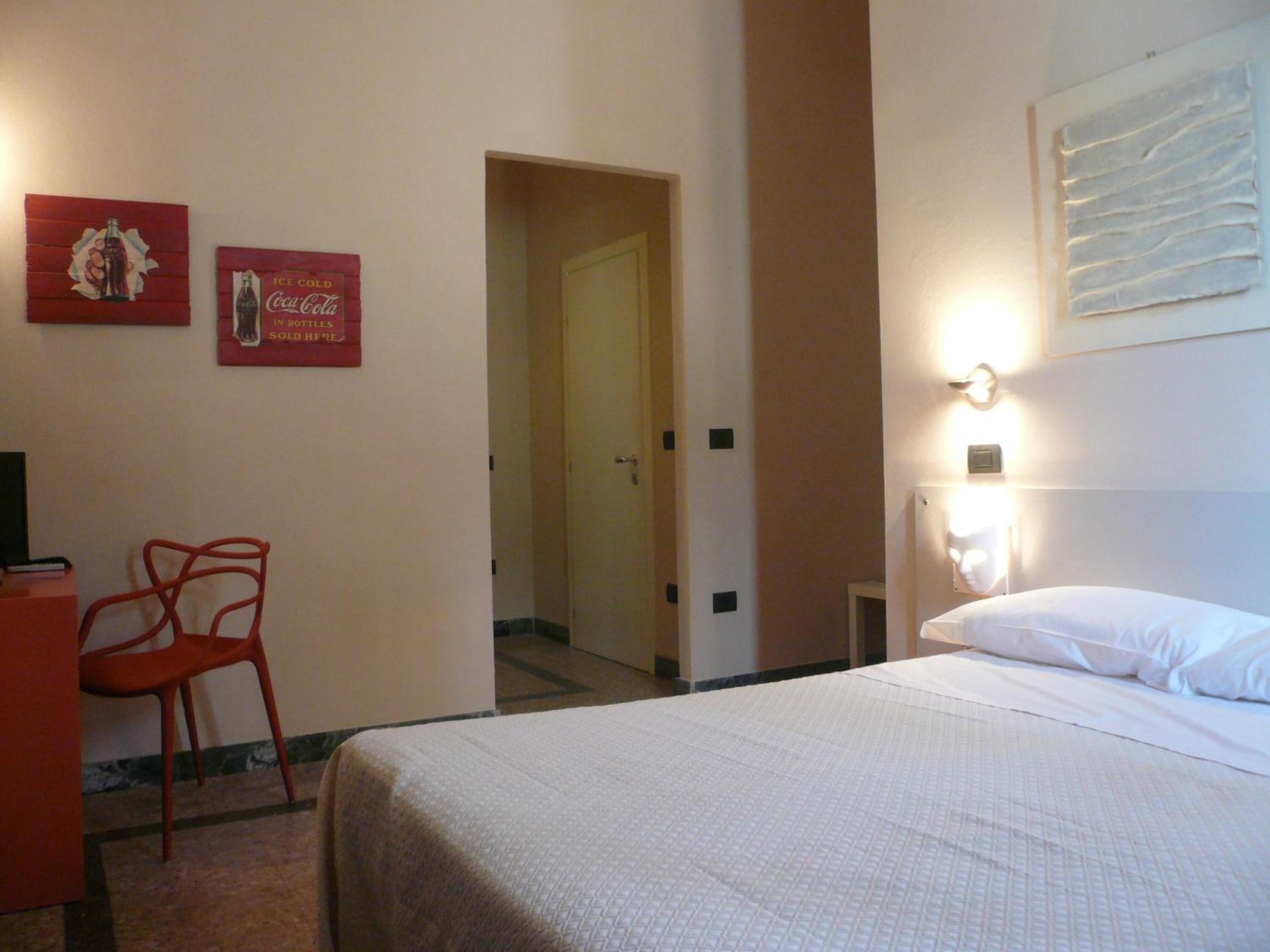 A hotel room with a bed, a chair, a desk, and two wall decorations.