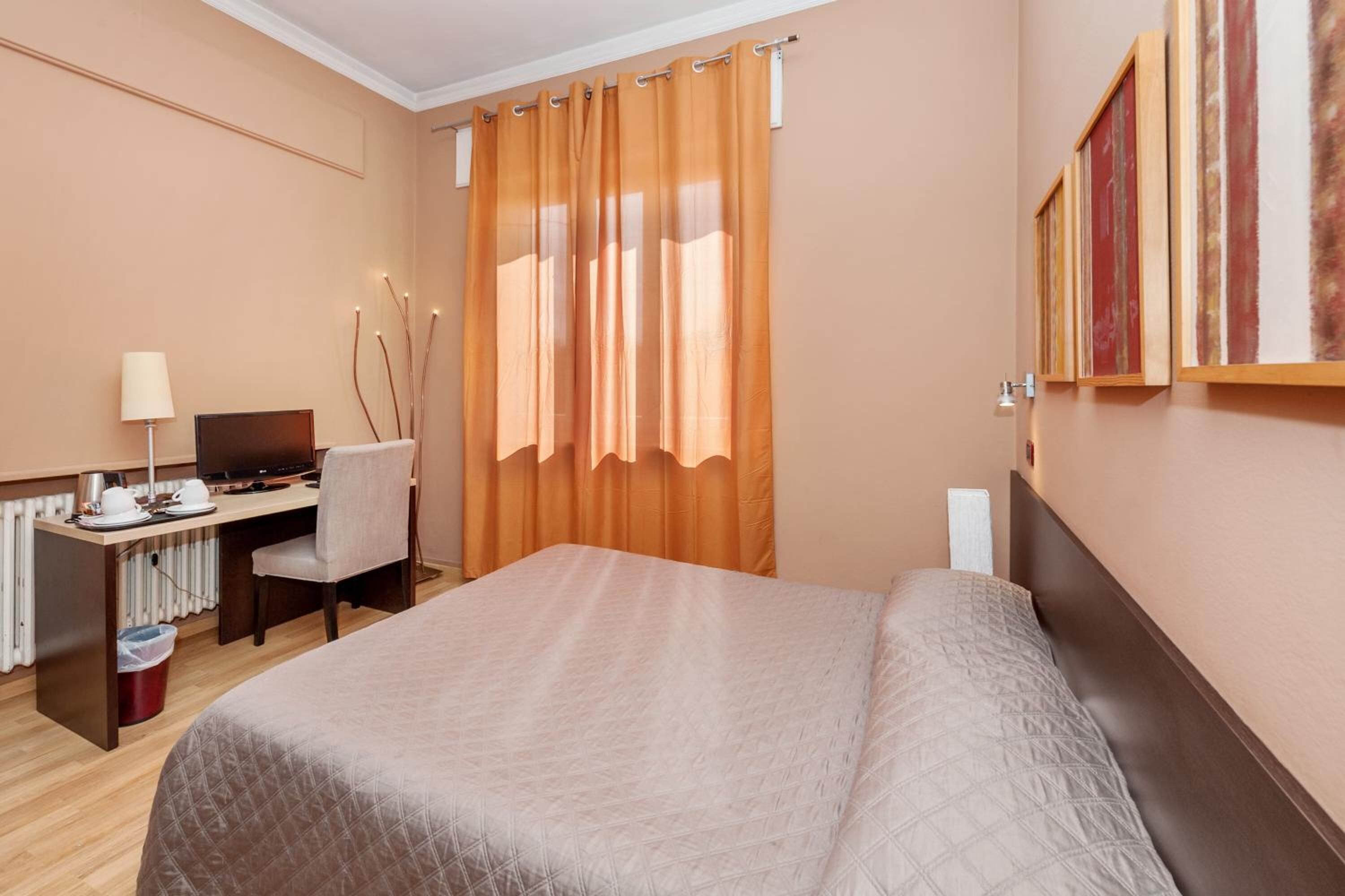 Habitación de hotel con cama, escritorio con computadora, silla y radiador.
