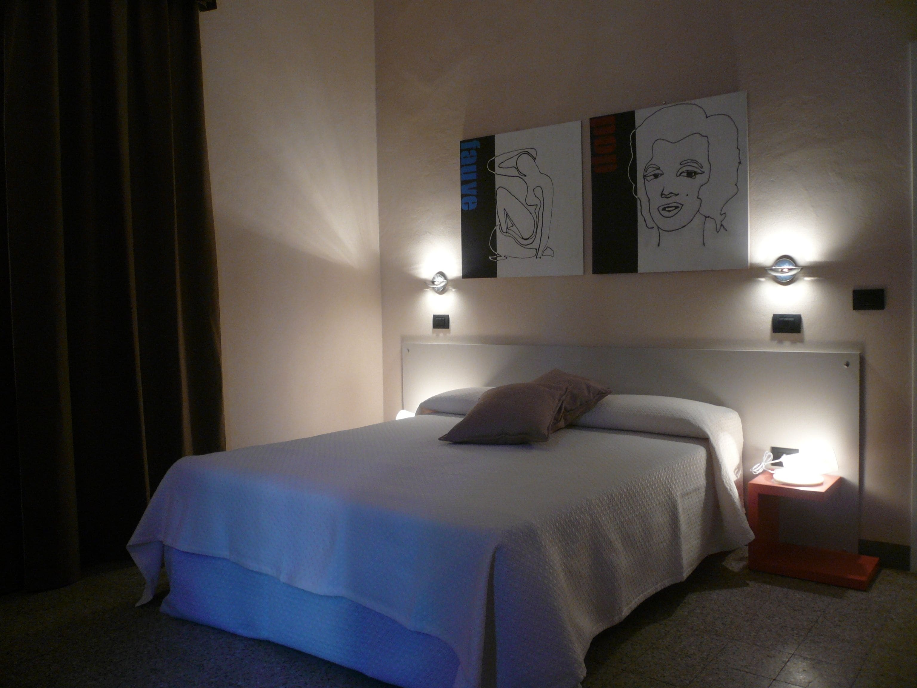 Una habitación de hotel con cama, mesita de noche y cuadros en la pared.