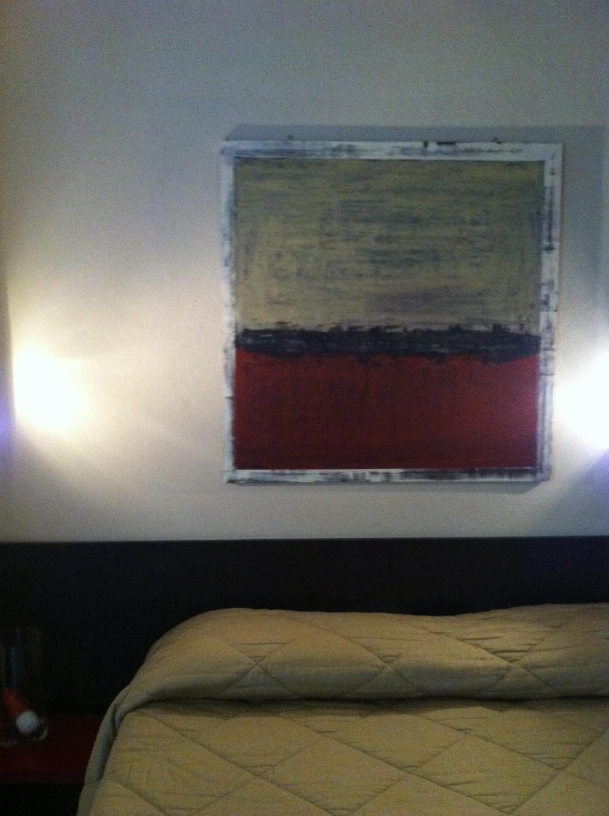 A room with a bed, a wall-mounted artwork, and a nightstand with a lamp.