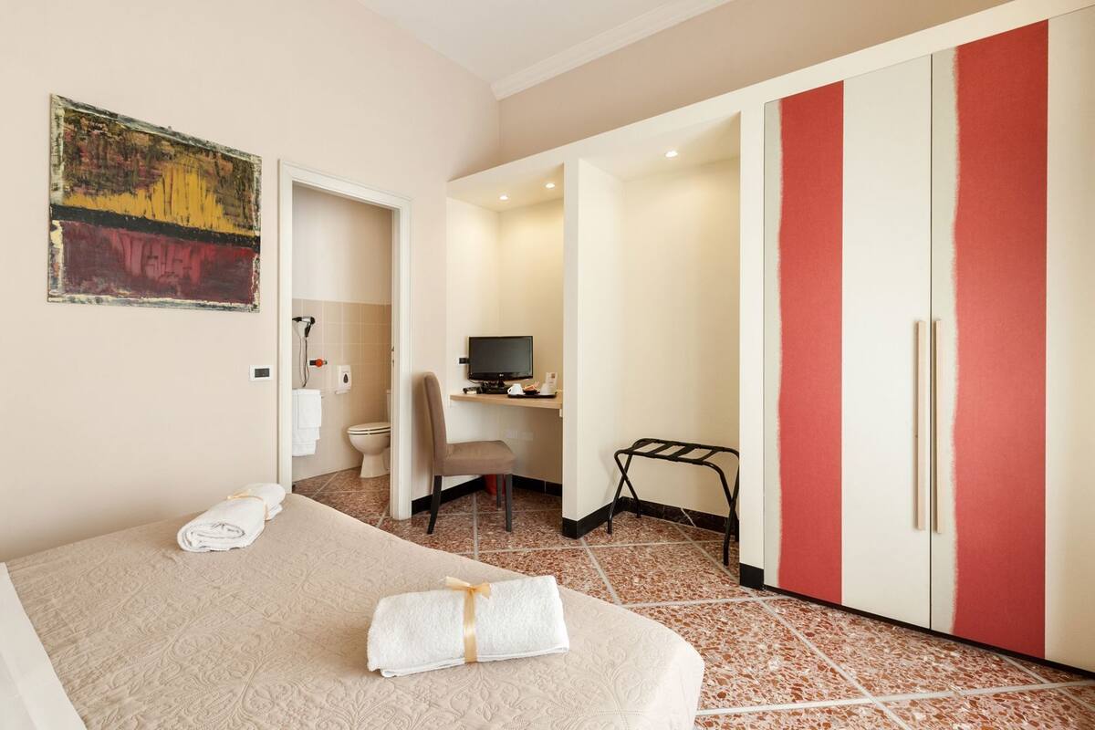 A hotel room with a bed, a desk with a computer, a chair, a wardrobe, and a bathroom.