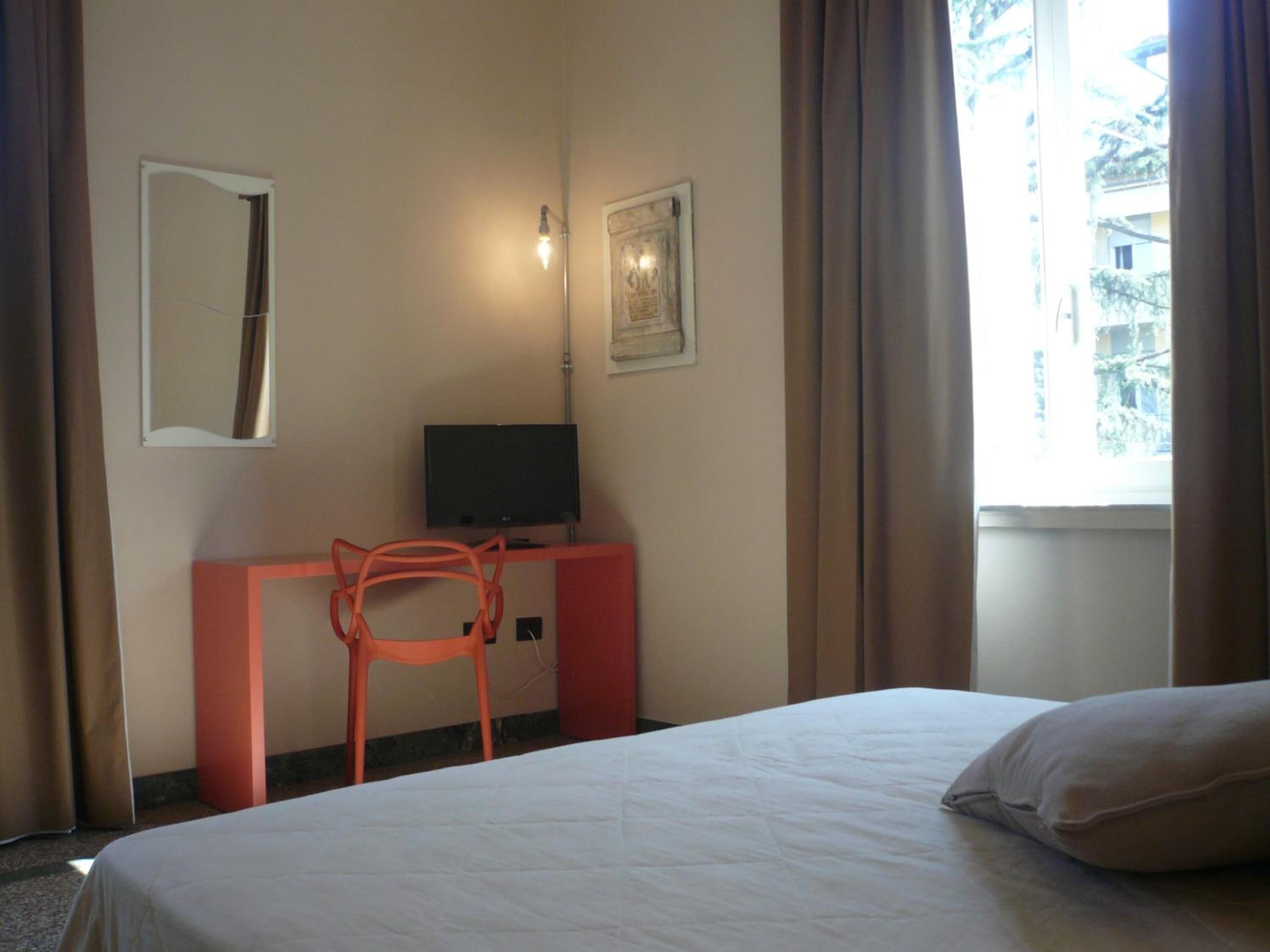 Habitación de hotel con cama, escritorio con silla, televisor, espejo y ventana con cortinas.