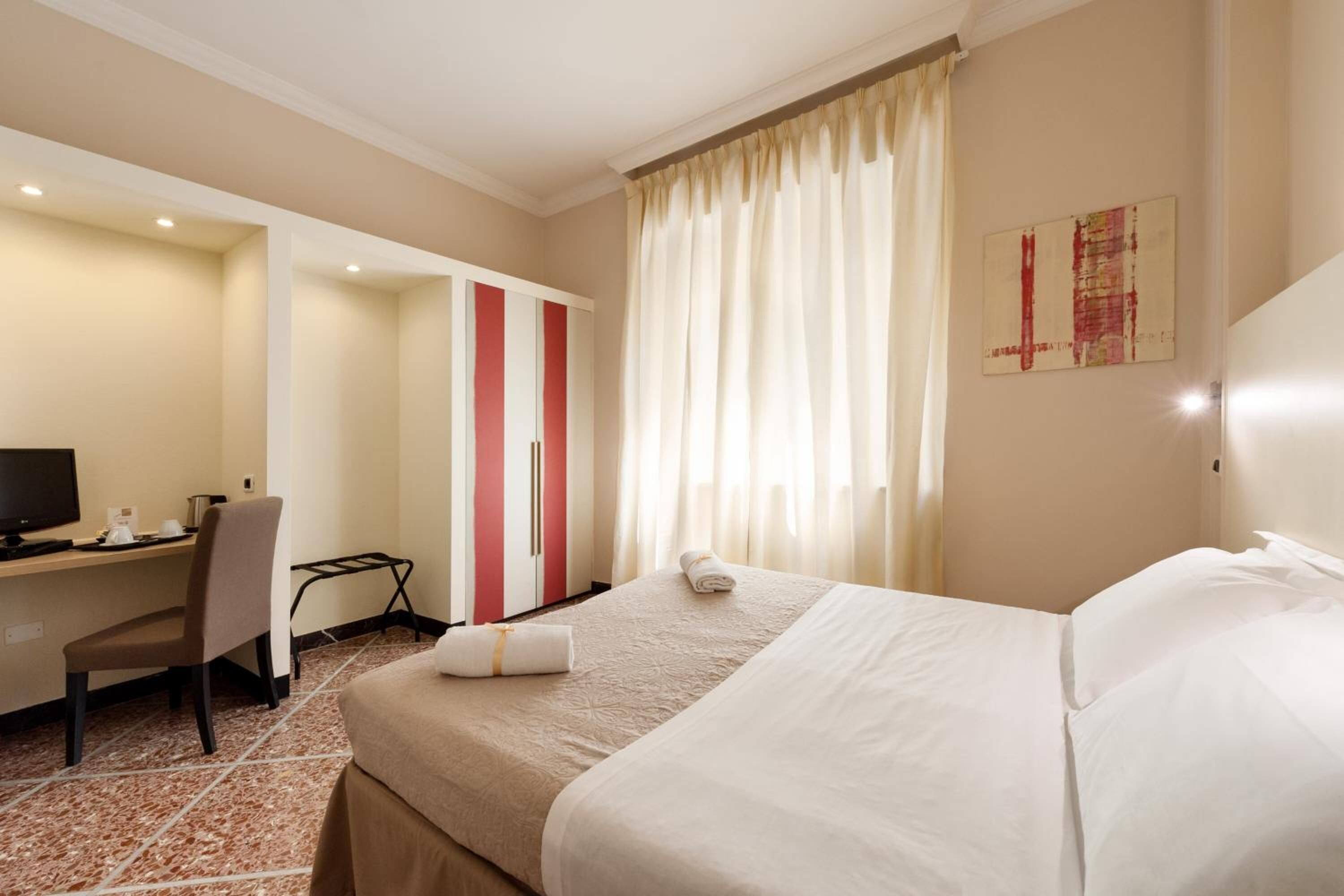 A hotel room with a bed, a desk, a chair, a television, and a window with curtains.