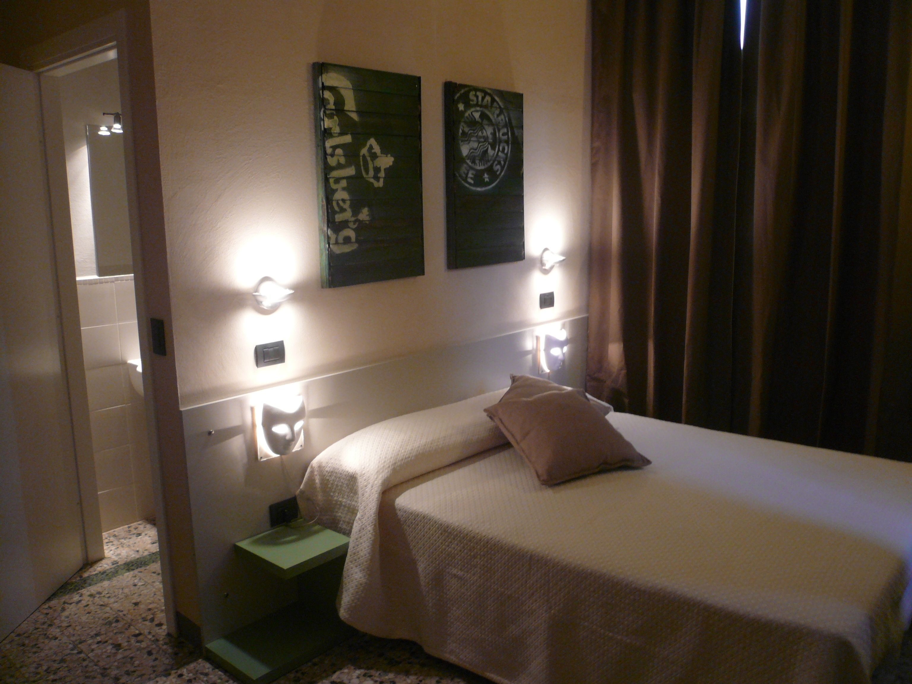 A hotel room with a bed, a nightstand, and two wall-mounted light fixtures.