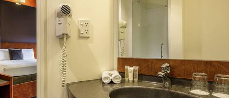 A hotel bathroom with a sink, mirror, hair dryer, and toiletries.