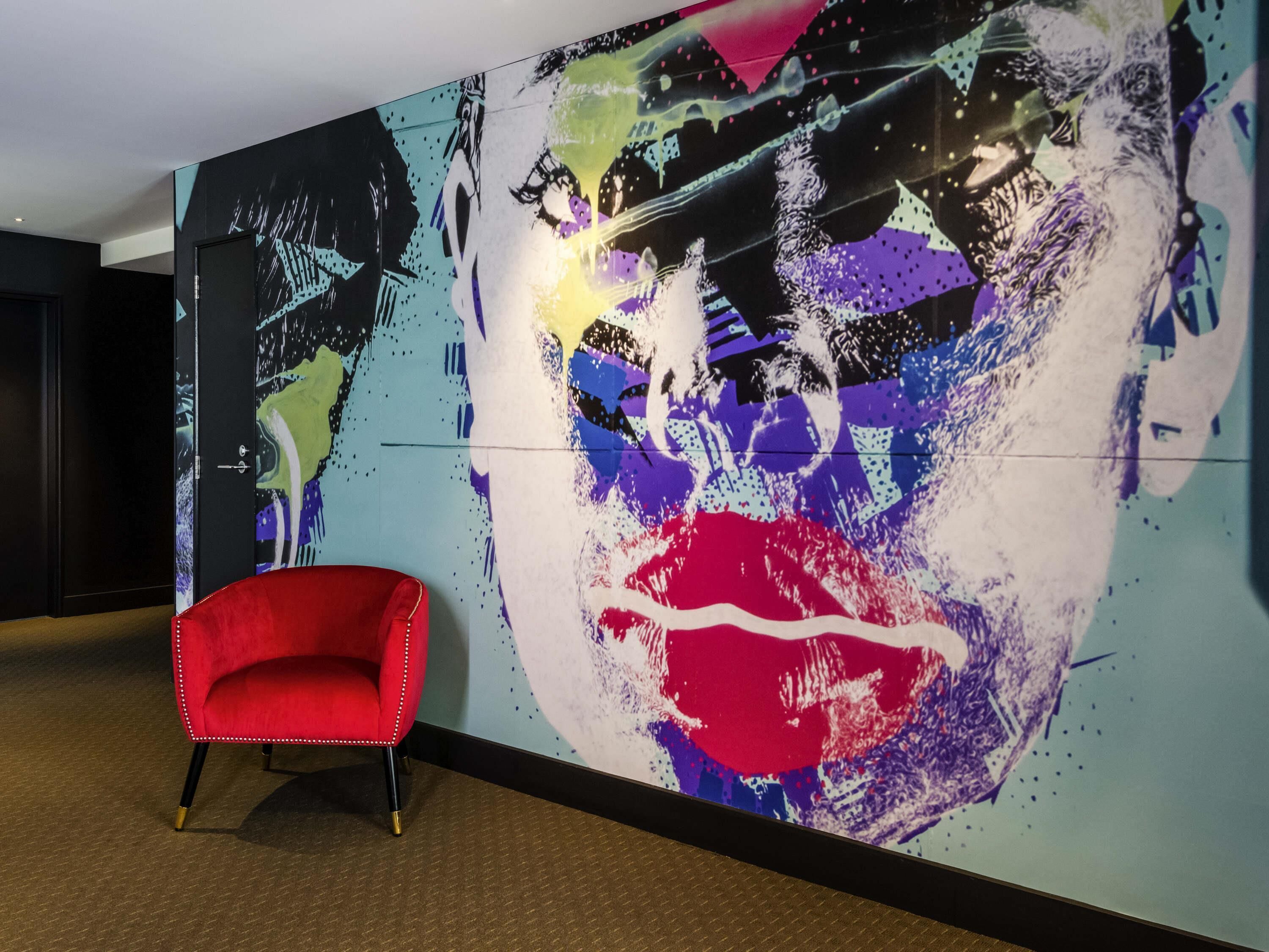 A red chair in a room with a large abstract painting on the wall.