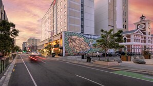 Ein modernes Hotel mit einer großen Wandmalerei, einem Uhrturm und einer Straße mit Autos.