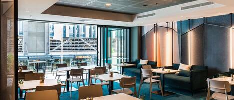 Un área de comedor moderna con mesas y sillas, vistas al exterior y un diseño de techo singular.