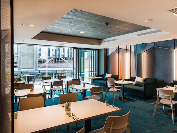 A modern dining area with tables and chairs, a view of the outside, and a unique ceiling design. - ibis Christchurch (Christchurch)