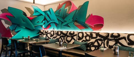 Un comedor moderno con arte abstracto en la pared, mesas de madera y sillas negras.