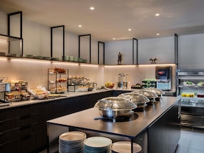Un buffet moderne avec différents postes de service pour les plats, une machine à café et un distributeur de boissons.