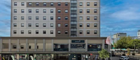 Un hotel de varios pisos con un llamativo logotipo de ibis, un restaurante y bar en la planta baja, y una calle peatonal frente al establecimiento.