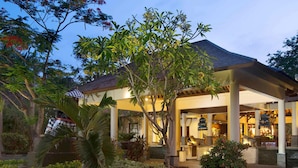 A well-lit hotel entrance with a covered patio, lush greenery, and a stone pathway leading to the entrance. - Novotel Bali Nusa Dua (Nusa Dua)