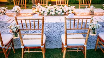 A table set with white tablecloths, wooden chairs, and floral centerpieces.