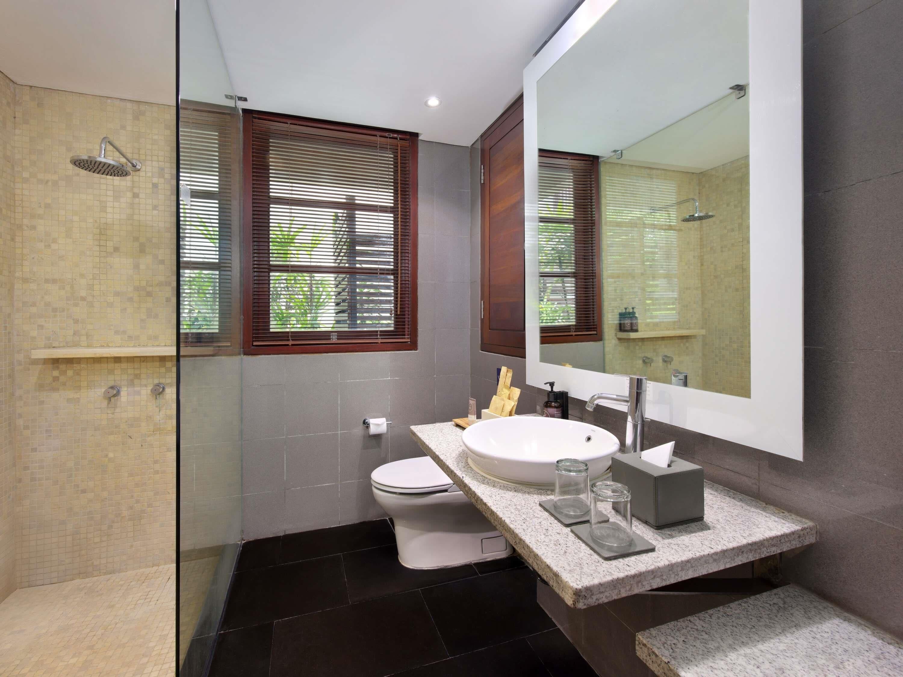 Un baño moderno con ducha envuelta en cristal, inodoro y lavamanos con un espejo grande.