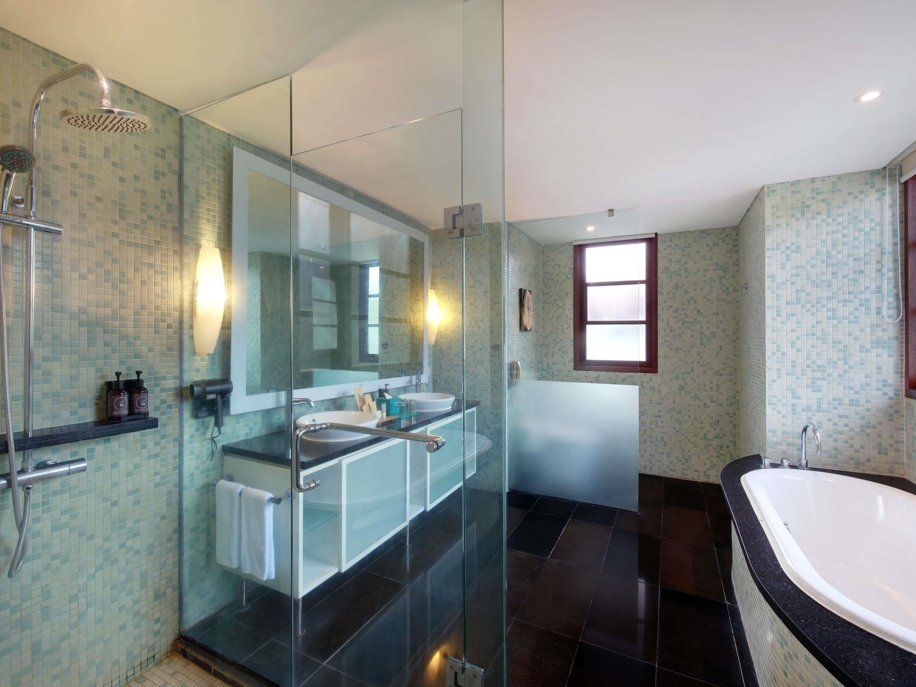 Une salle de bain moderne dotée d’une douche à parois de verre, de deux vasques, d’une grande baignoire et d’une fenêtre laissant entrer la lumière naturelle.
