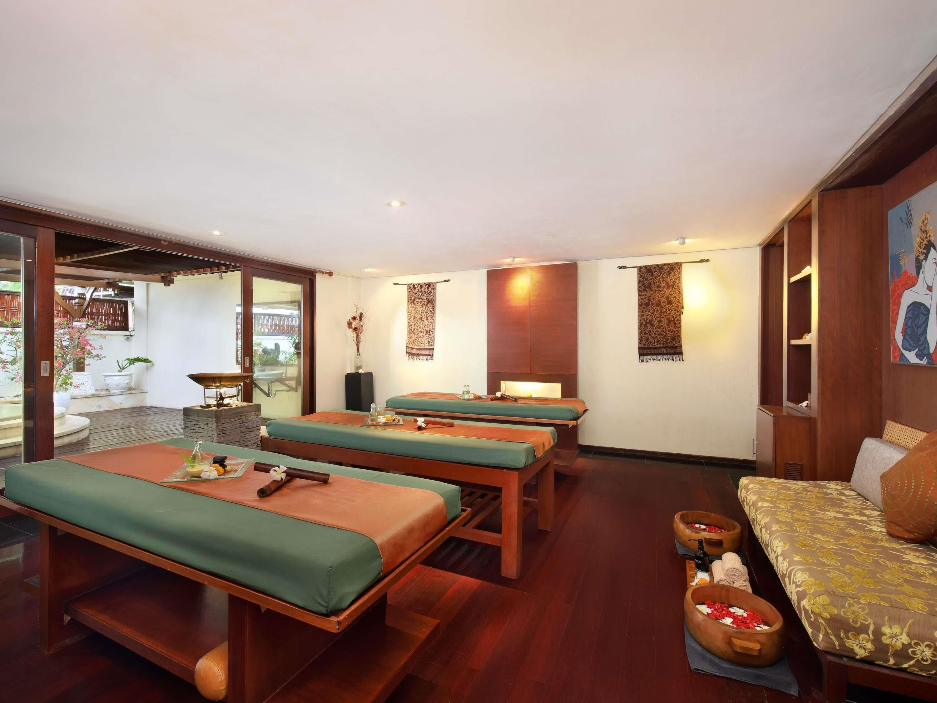 A spa room with wooden massage tables, a sofa, and a small altar with flowers.
