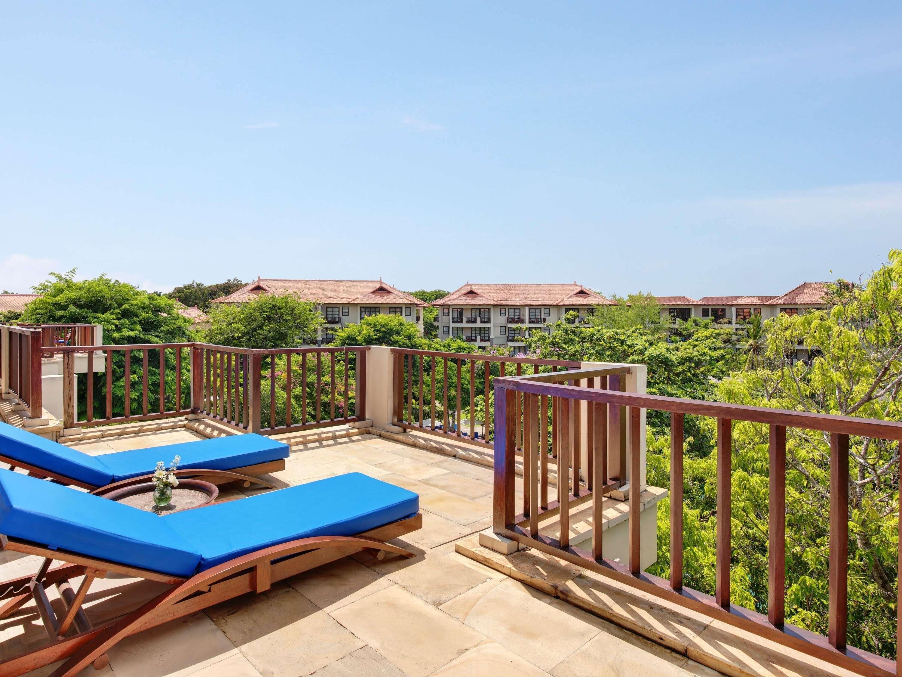 A balcony with blue lounge chairs and a view of a residential area with houses.