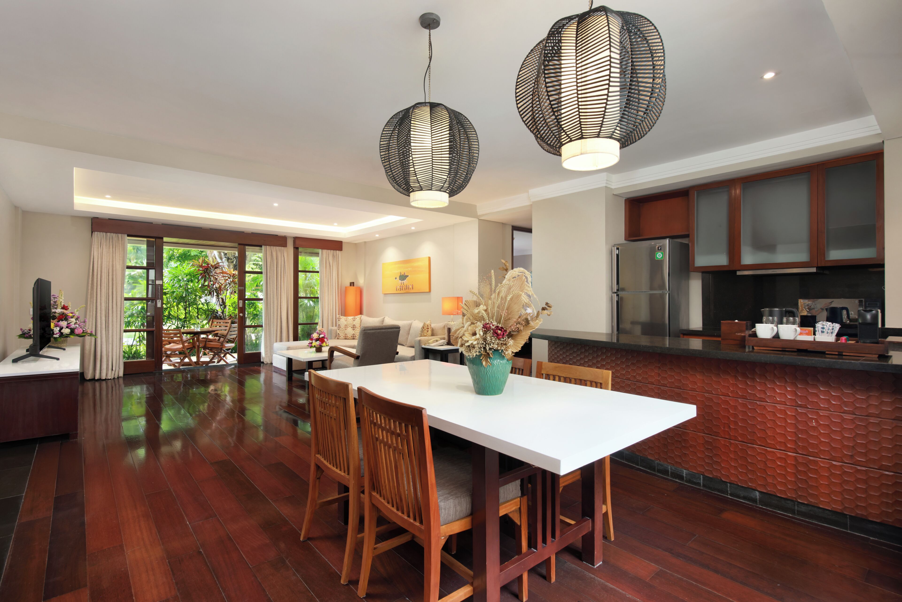 A spacious living area with a dining table, wooden chairs, and a kitchen area with a refrigerator and cabinets.
