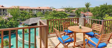A balcony with a wooden table and chairs, overlooking a pool and lush greenery.