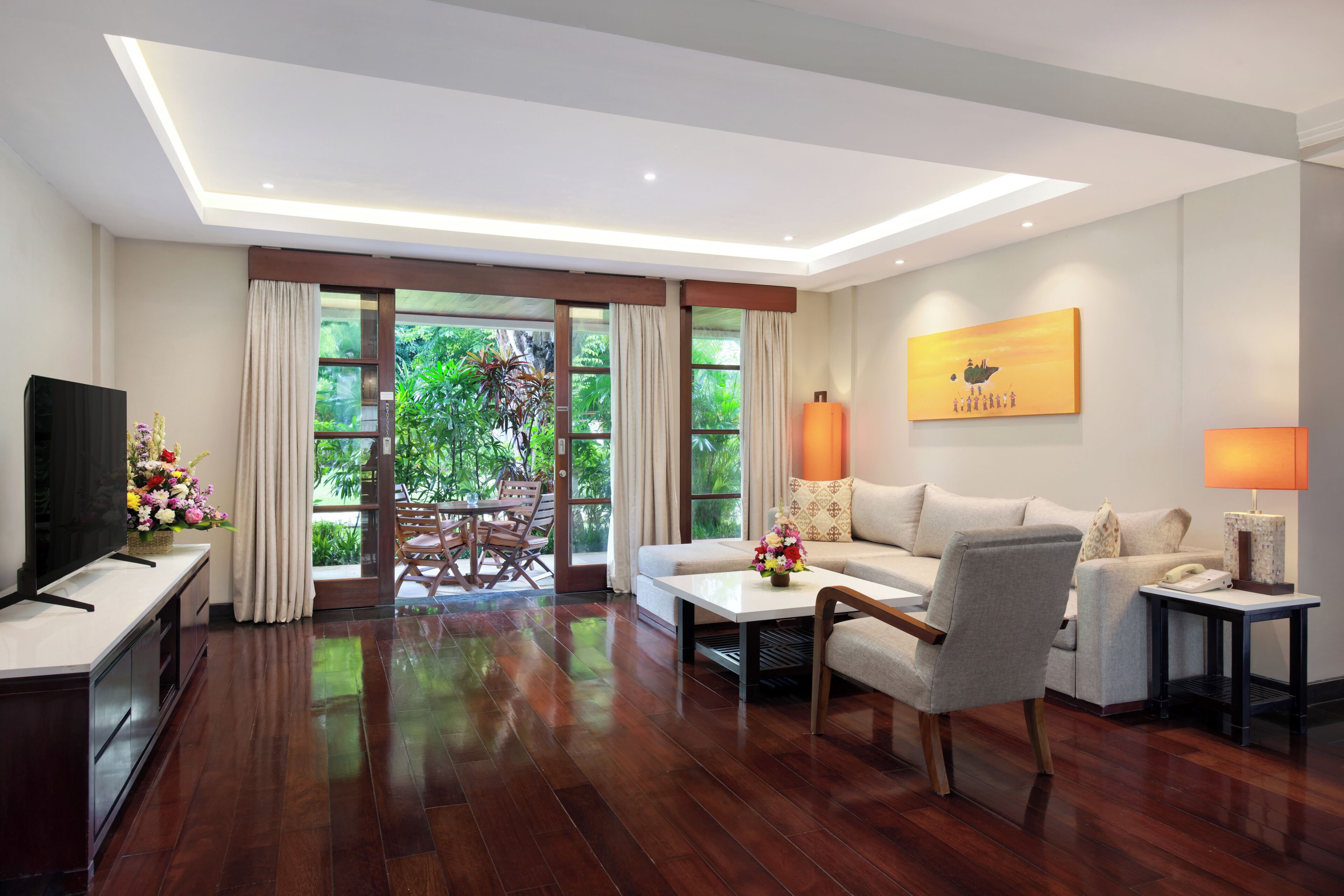 A modern living room with a sofa, armchairs, a coffee table, and a TV. There is a dining area with a table and chairs.