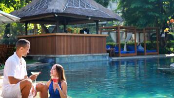 A pool area with a thatched-roof structure, lounge chairs, and a clear pool.