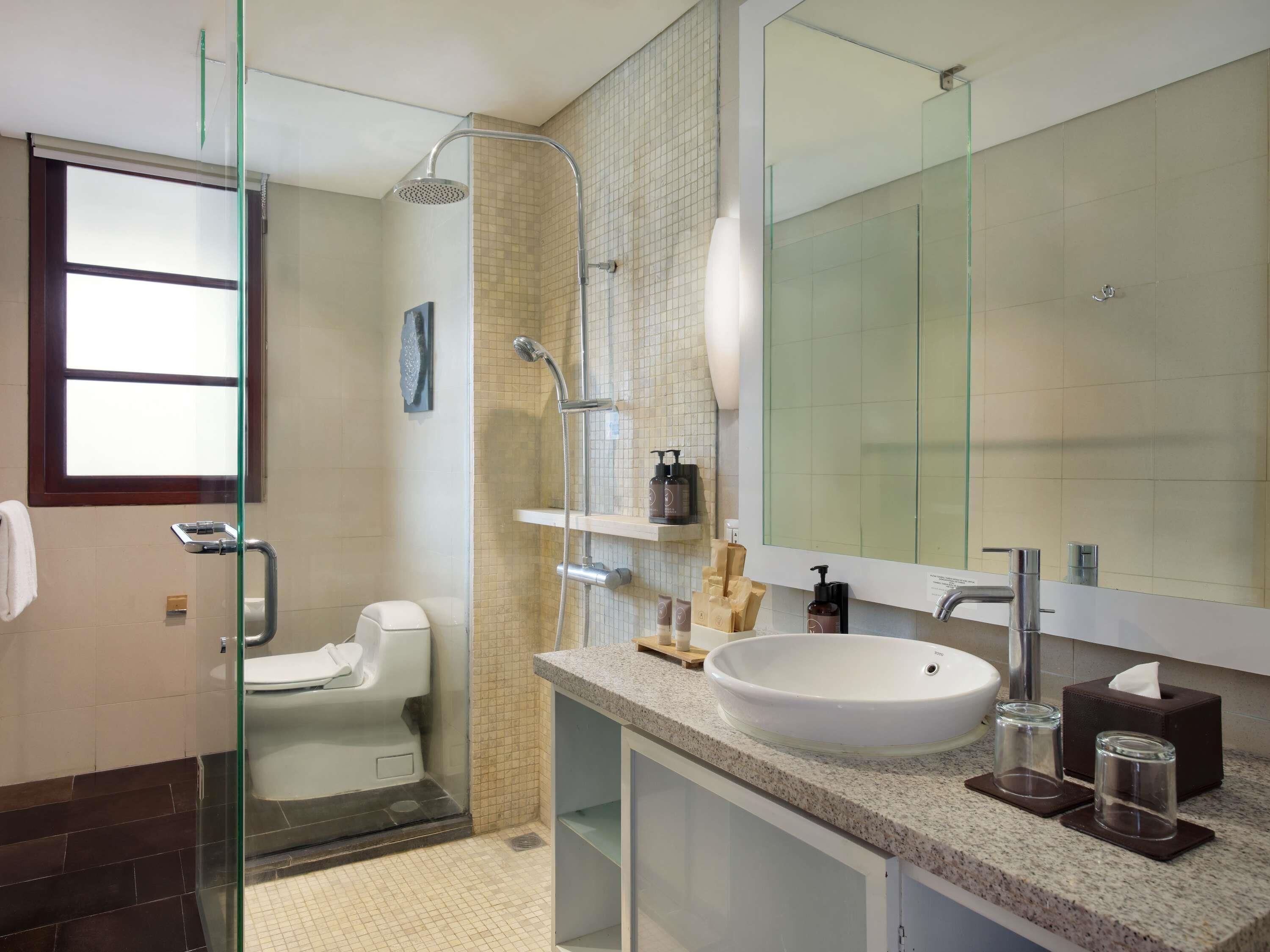 Un baño moderno con cabina de ducha de vidrio, inodoro, lavabo con un espejo grande y artículos de aseo en la encimera.